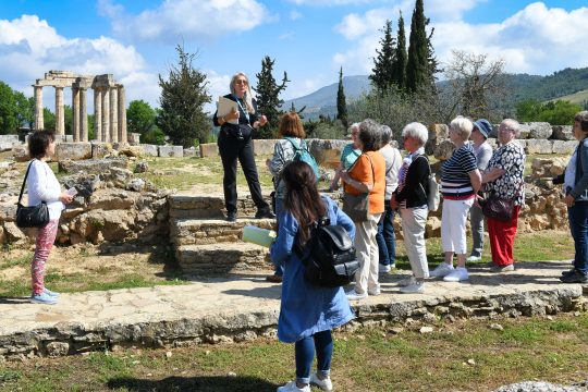 eine Reiseführerin erläutert einer Gruppe von Menschen etwas mit Blick auf antike Bauten
